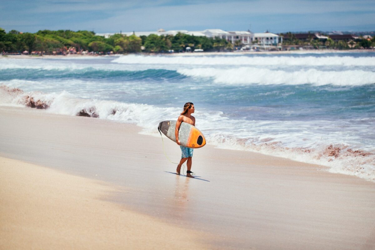 man carrying yellow and white surfboard standing near beach